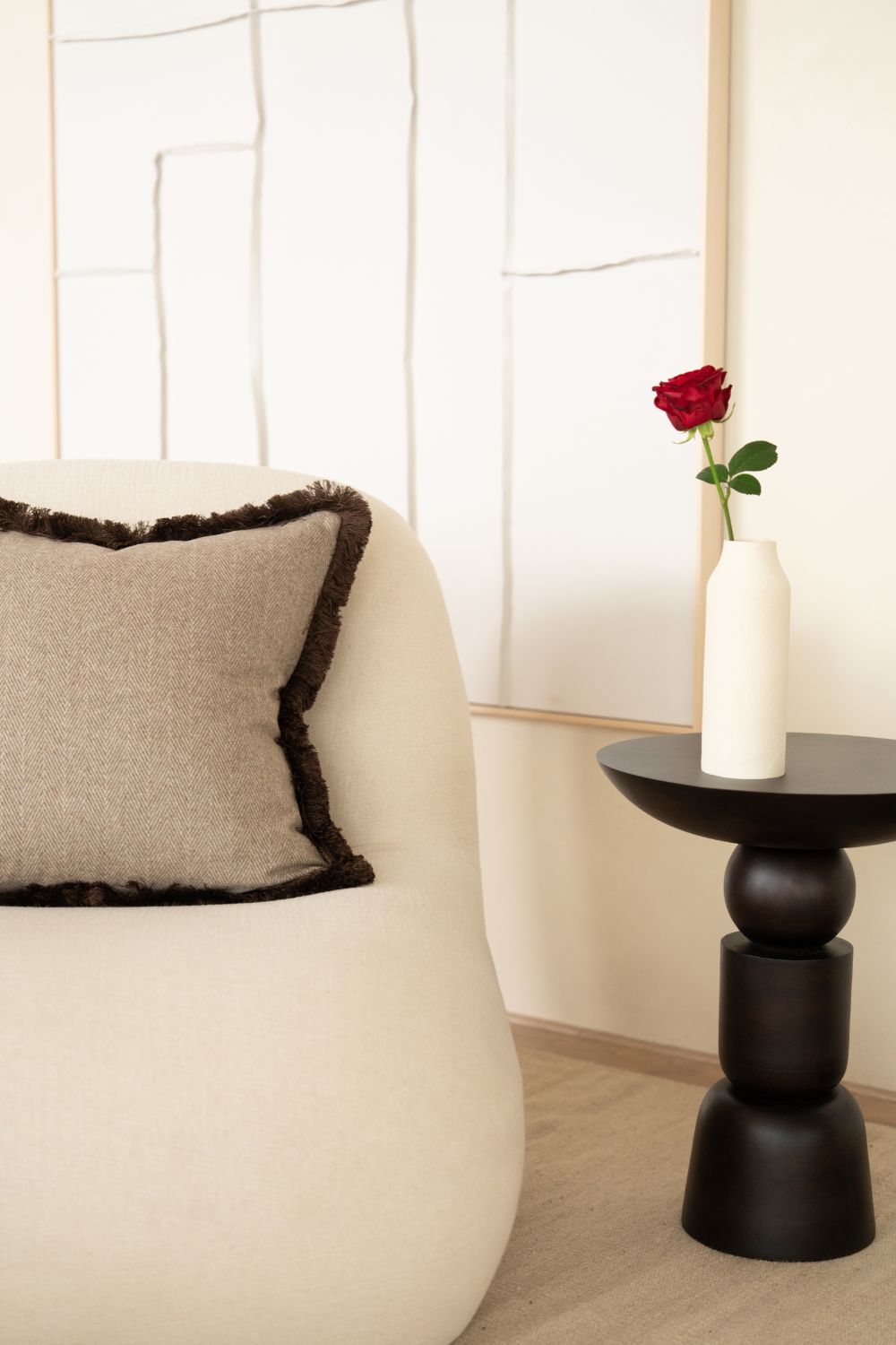 Beige sierkussen met visgraatmotief en bruine franjes ligt op een fauteuil