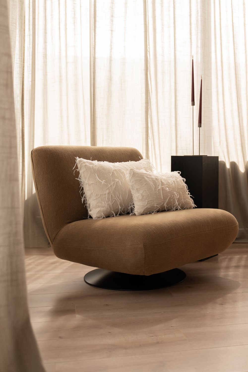 Twee ivoorwitte sierkussens liggen op een bruine fauteuil. De sierkussens zijn uniek en hebben loshangende garen.