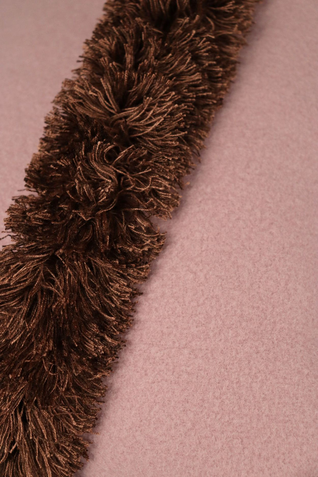 Een close up foto van een roze sierkussen met lichtbruine franjes.