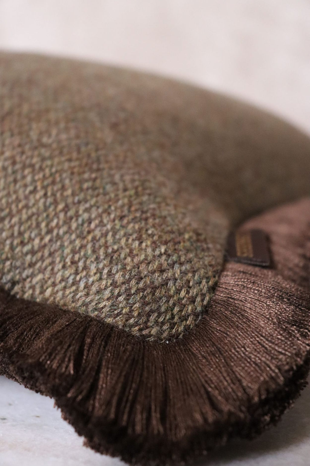 Een close up afbeelding van de groene wollen stof van een sierkussen met bruine franjes.