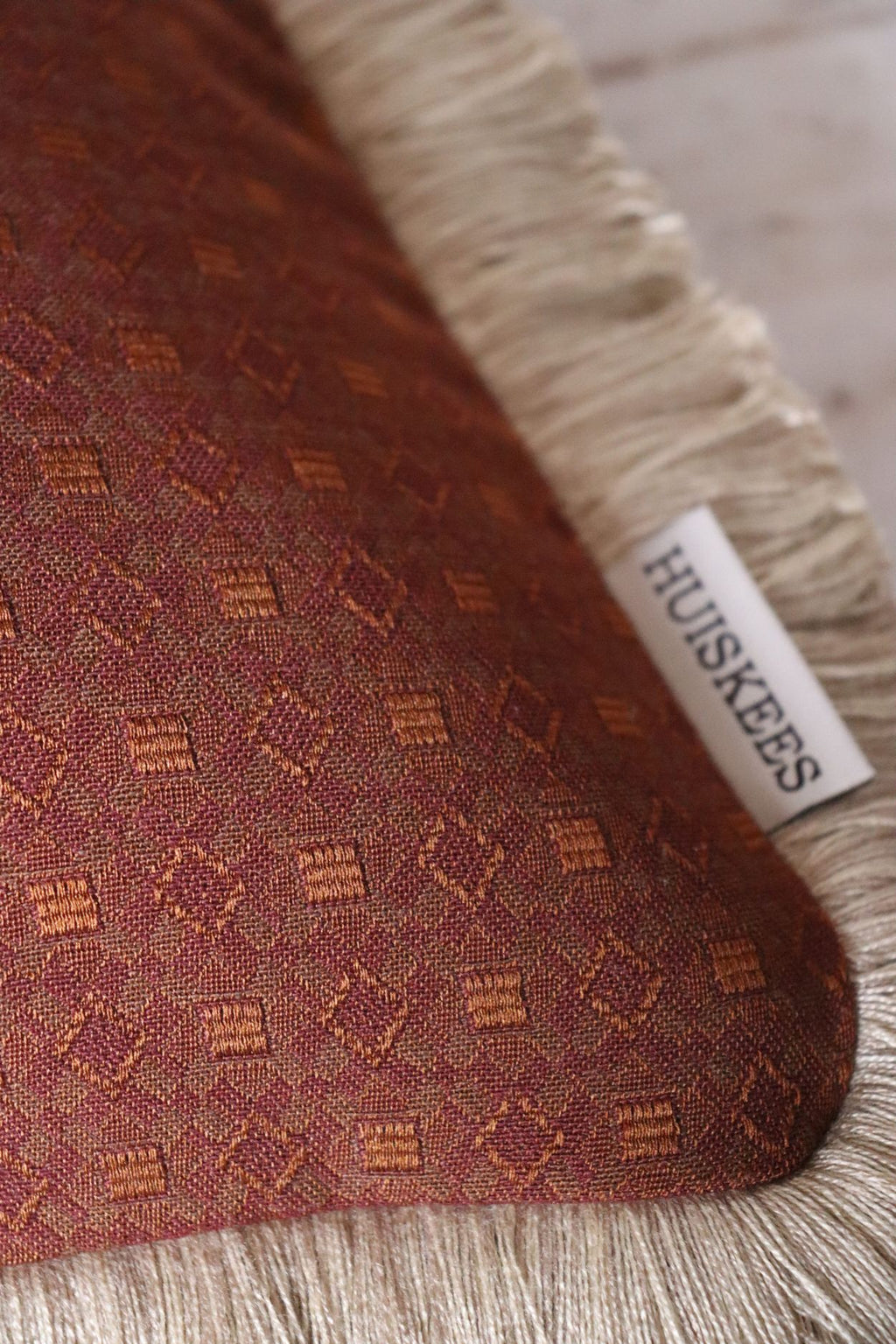 Een close up van een oranje sierkussen met beige franjes.