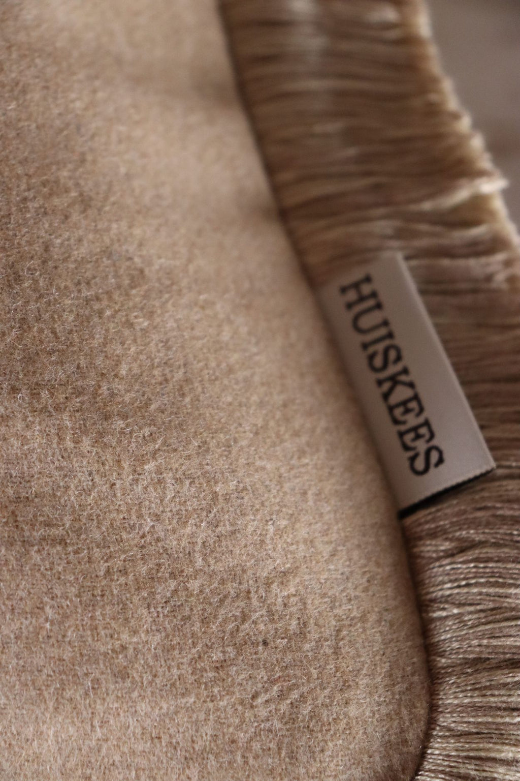 De stof van een beige sierkussen met franjes gemaakt van wol.