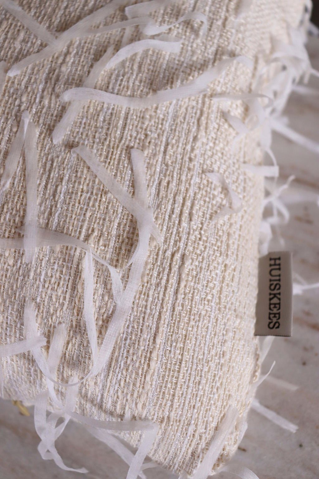 De stof van een uniek wit sierkussen met losse draden.