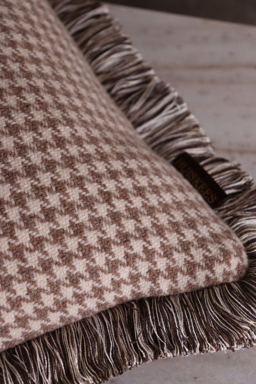 De stof van een sierkussen met een beige pied-de-poule motief en franjes.