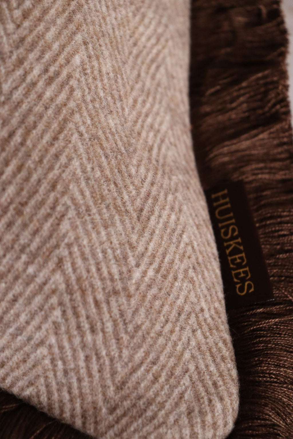 De stof van een wollen beige-bruin sierkussen met bruine franjes.