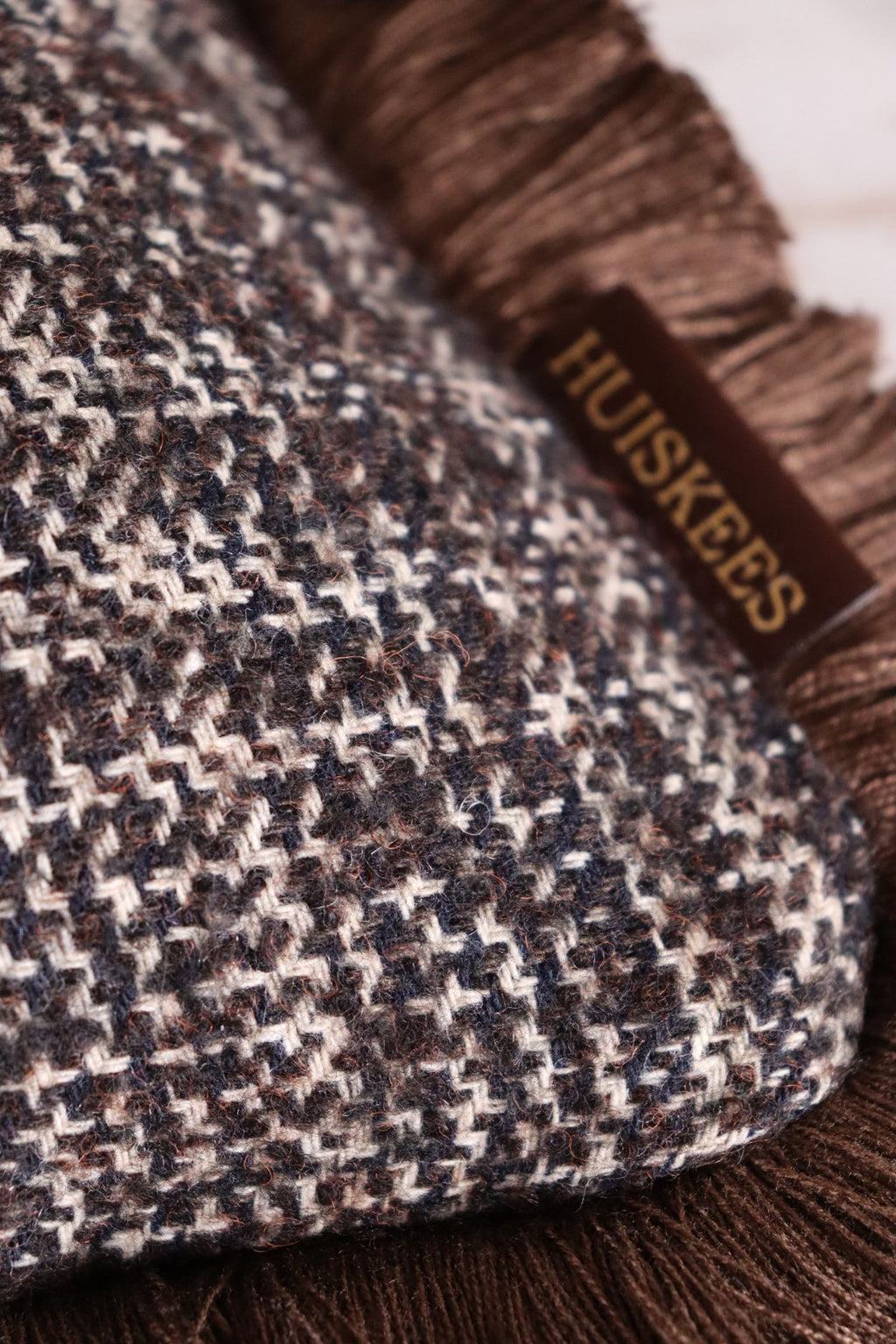 De stof van een wollen donkerbruin sierkussen met franjes.