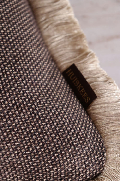 De stof van een bruin sierkussen met subtiele beige stippels en een beige franjeband.