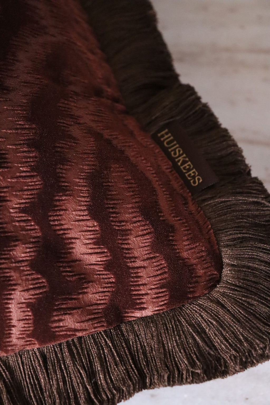 Een close up van een donkerroze sierkussen met bruine franjes.