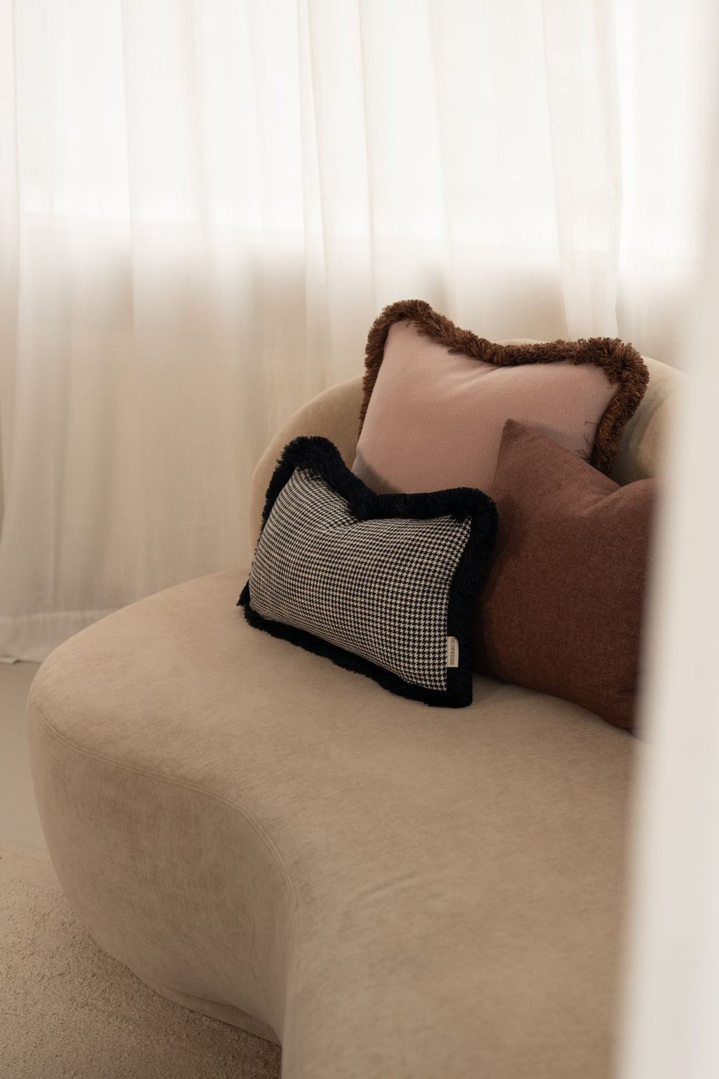 Drie kussens liggen op een beige bank.