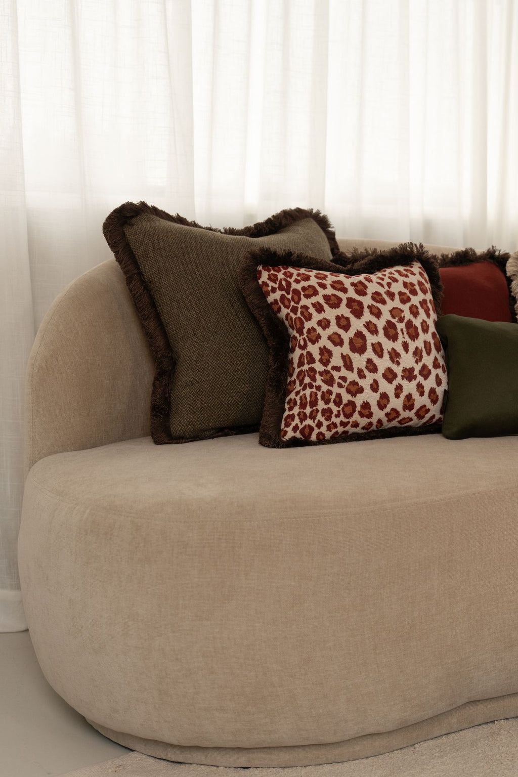 Een donkergroen kussen en een rood kussen met luipaardmotief liggen op een beige bank.