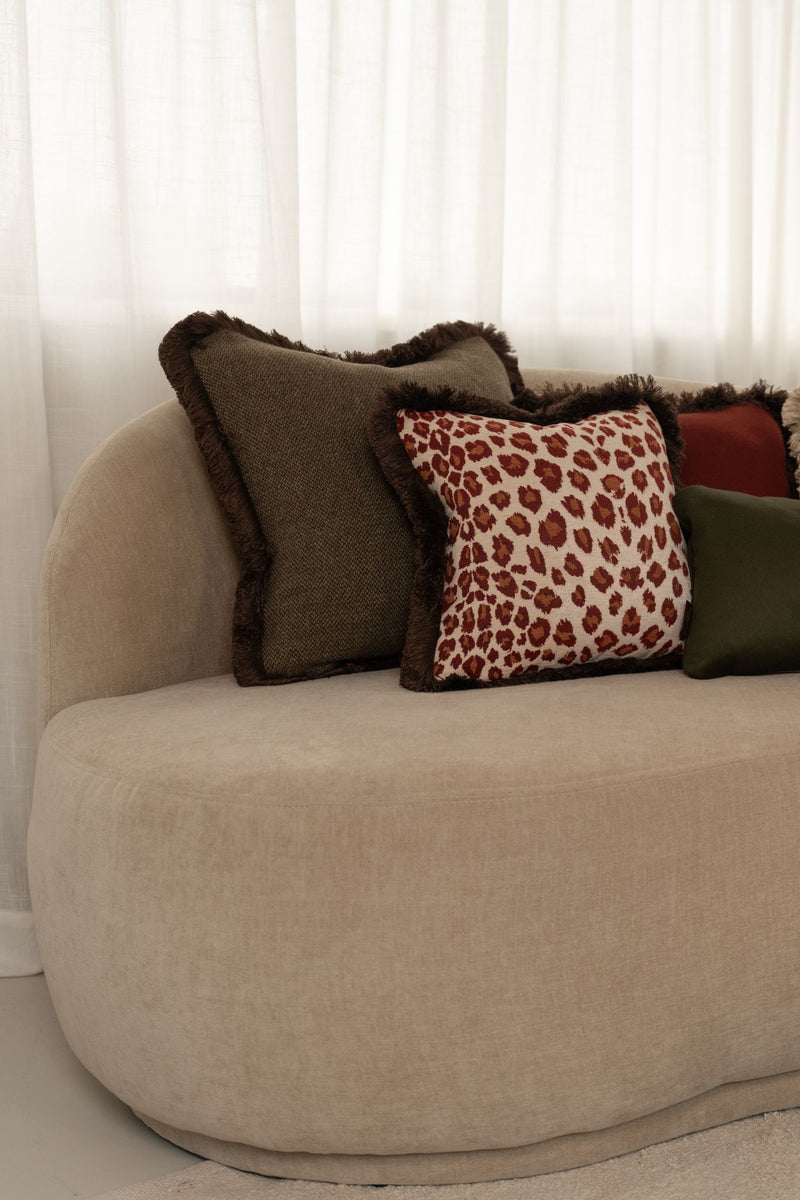 Een donkergroen kussen en een rood kussen met luipaardmotief liggen op een beige bank.
