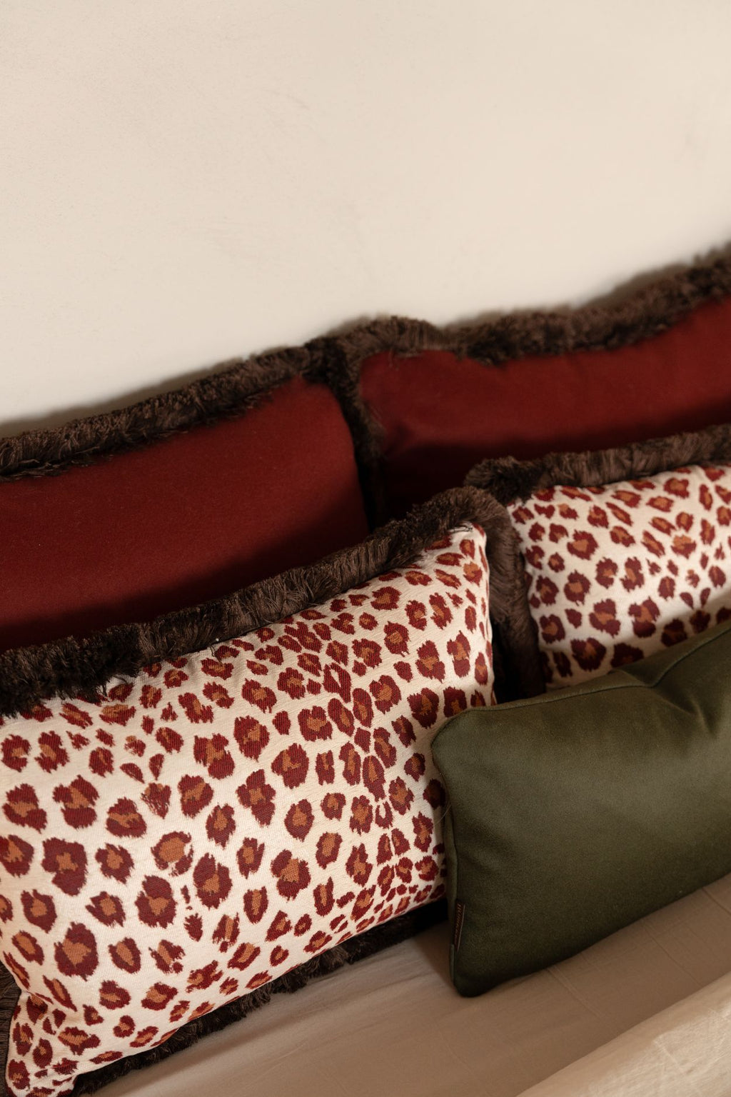 Rode sierkussens met franjes en luipaardmotief liggen op bed.