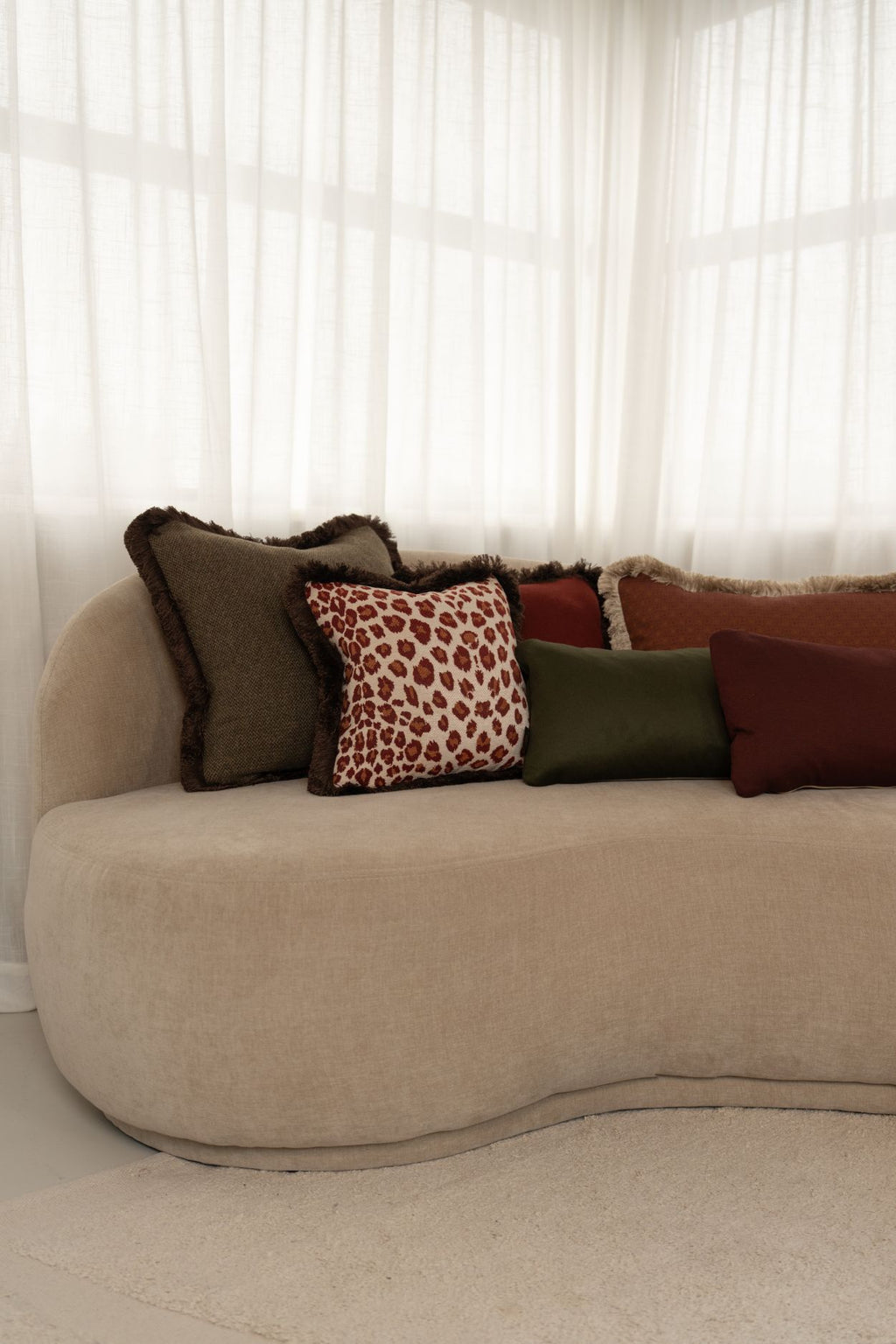 Luxe groene, rode en oranje sierkussens met franjes liggen op een beige bank.