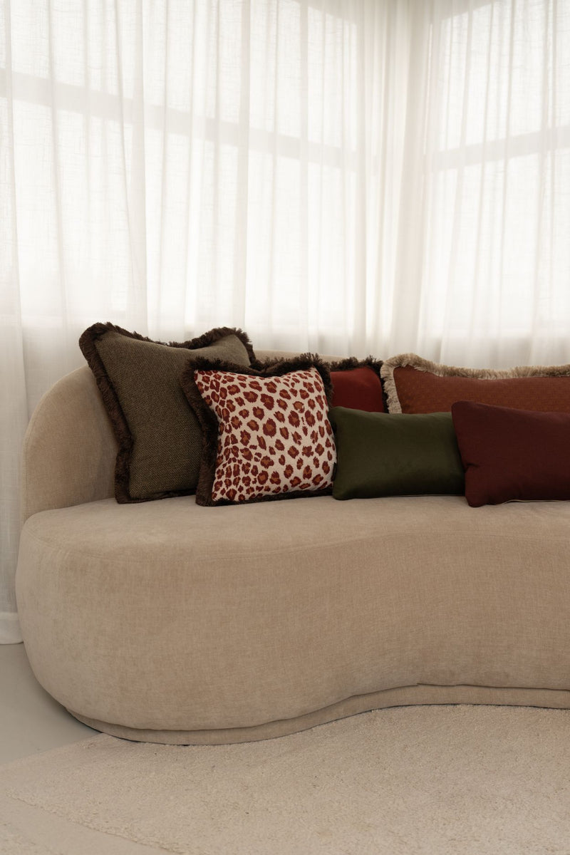 Luxe groene, rode en oranje sierkussens met franjes liggen op een beige bank.