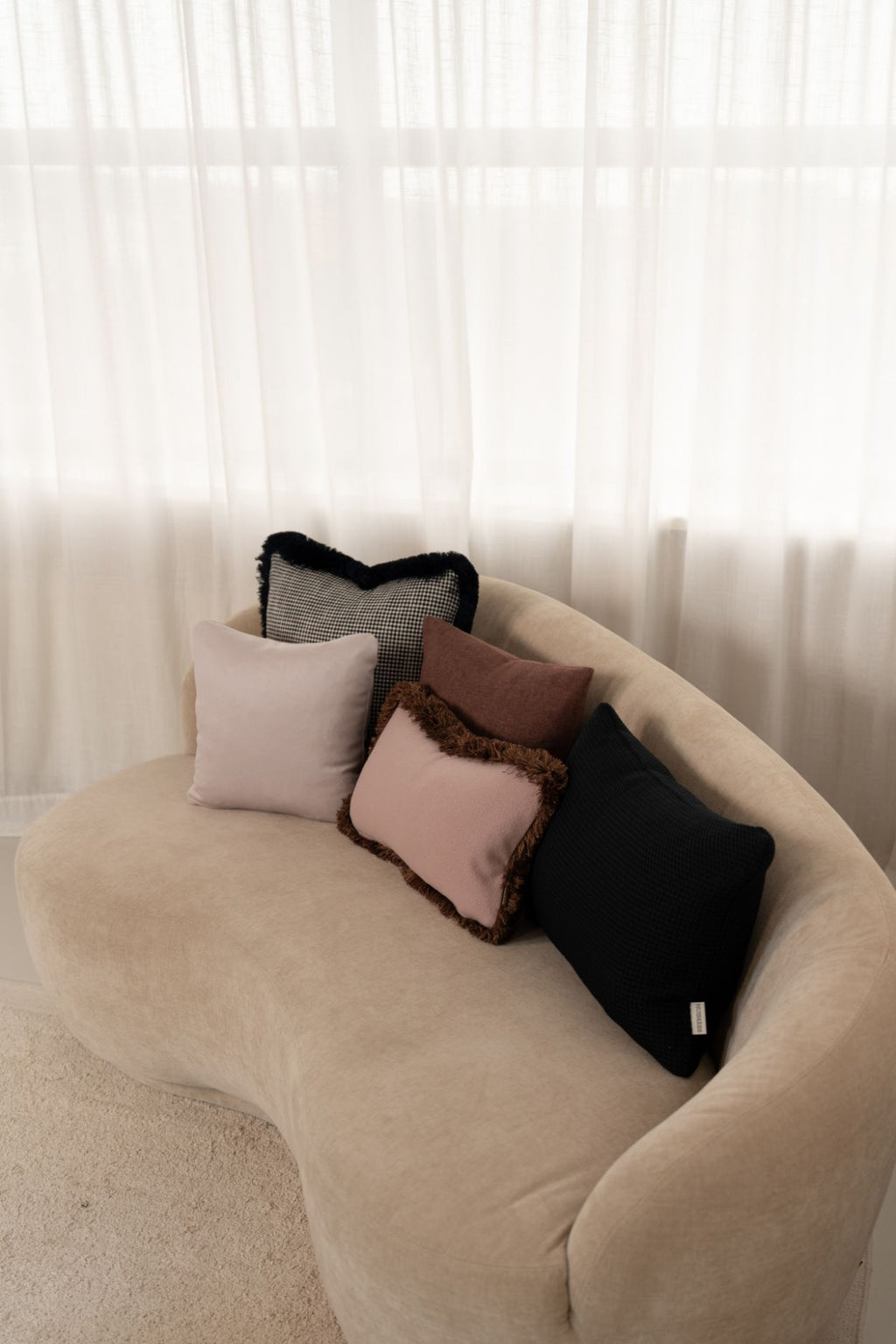 Roze en blauwe sierkussens met en zonder franjes liggen op een beige bank.