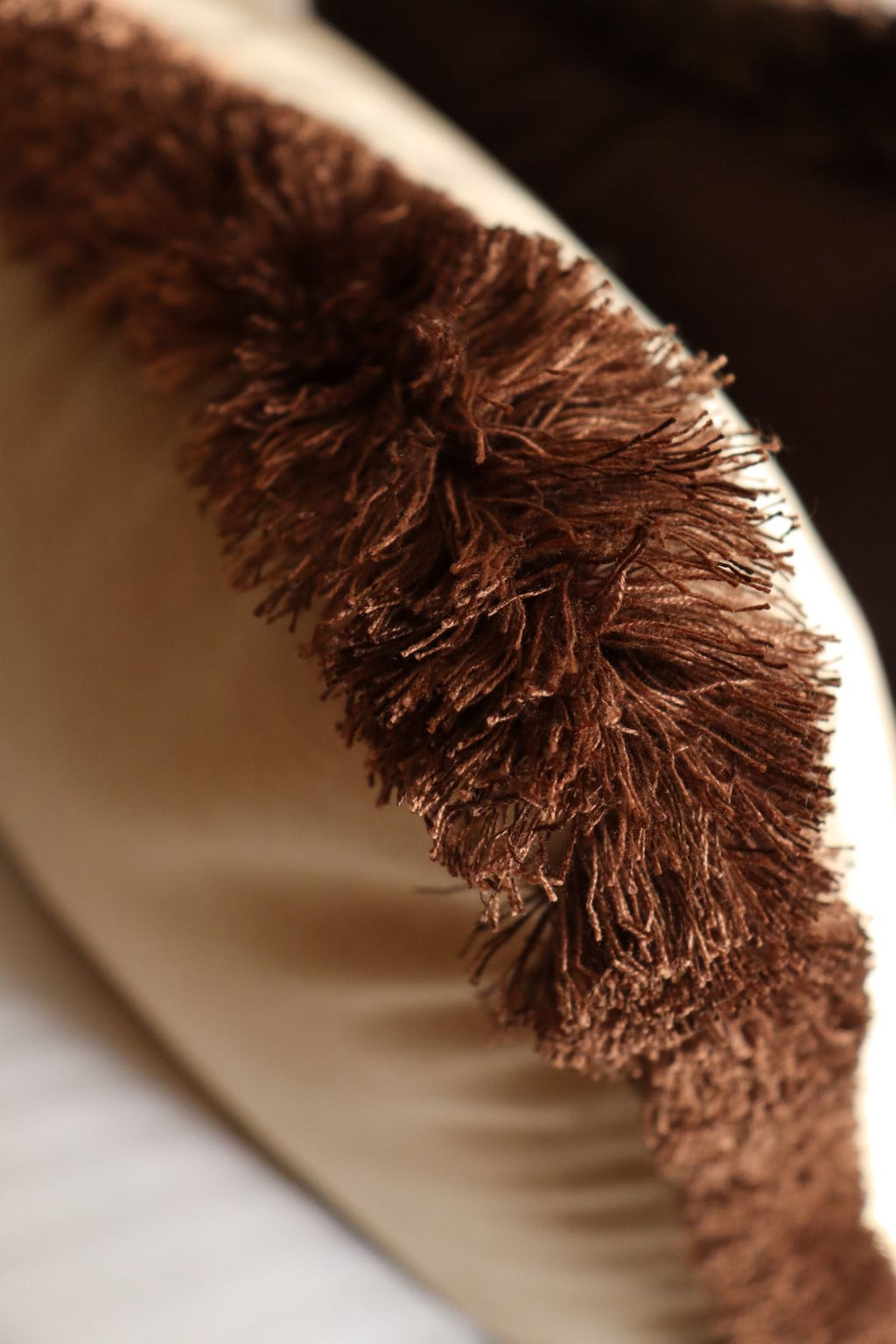Lichtbruine franjes van een beige sierkussen op bed.