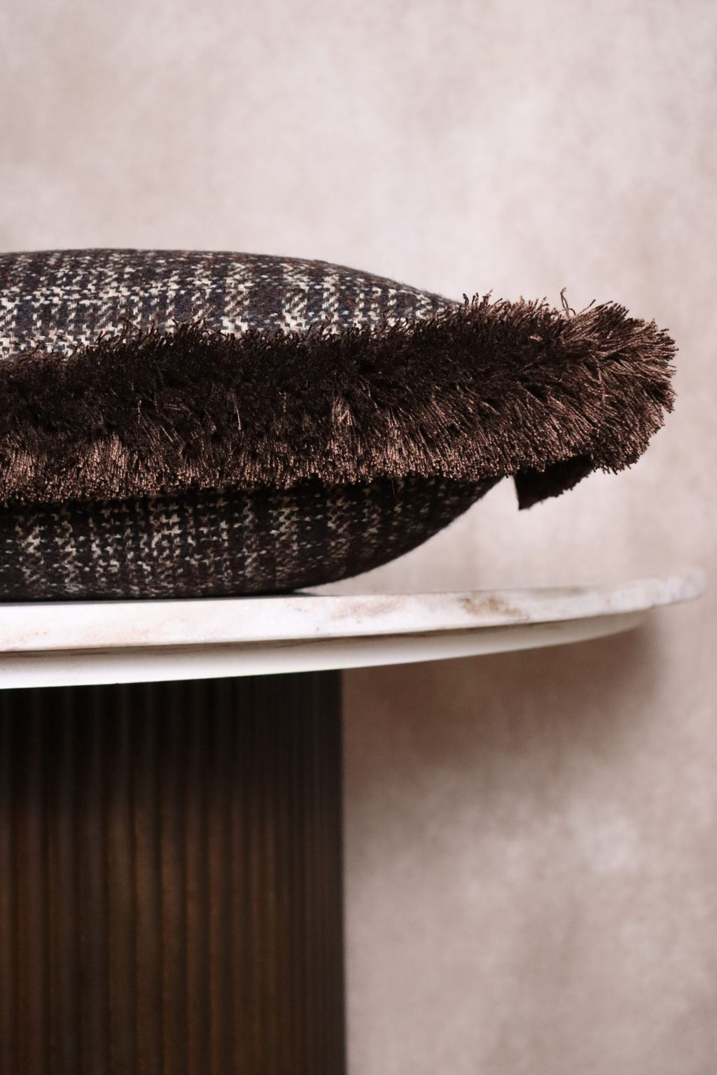 Een bruin sierkussen ligt op een tafeltje zodat de bruine franjes goed zichtbaar zijn.