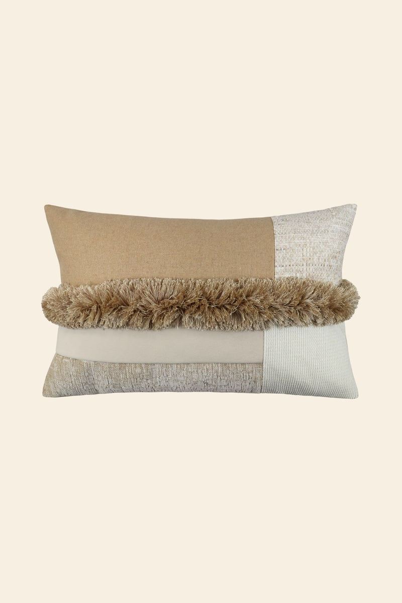 De voorkant van een beige sierkussen met verschillende stoffen en franjes in het midden.