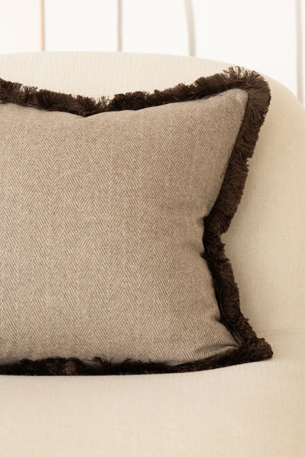 Beige sierkussen met bruine franjes ligt op een fauteuil