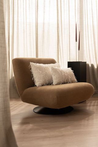 Twee ivoorwitte sierkussens liggen op een bruine fauteuil. De sierkussens zijn uniek en hebben loshangende garen.