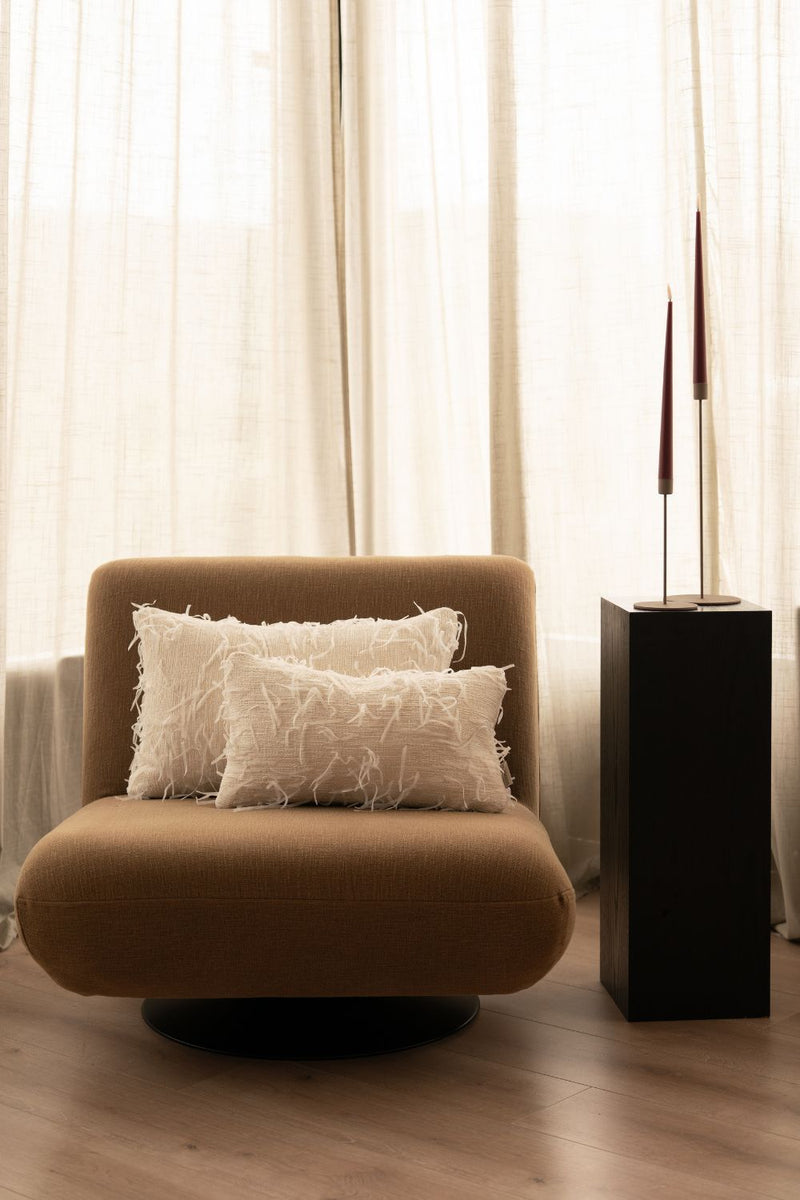 Twee crèmekleurige sierkussens met losse garen liggen op een bruine fauteuil.