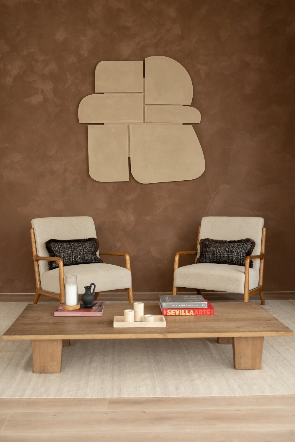 Twee fauteuils staan in een rustgevende ruimte. Op de witte fauteuils liggen bruine sierkussens met bruine franjes.