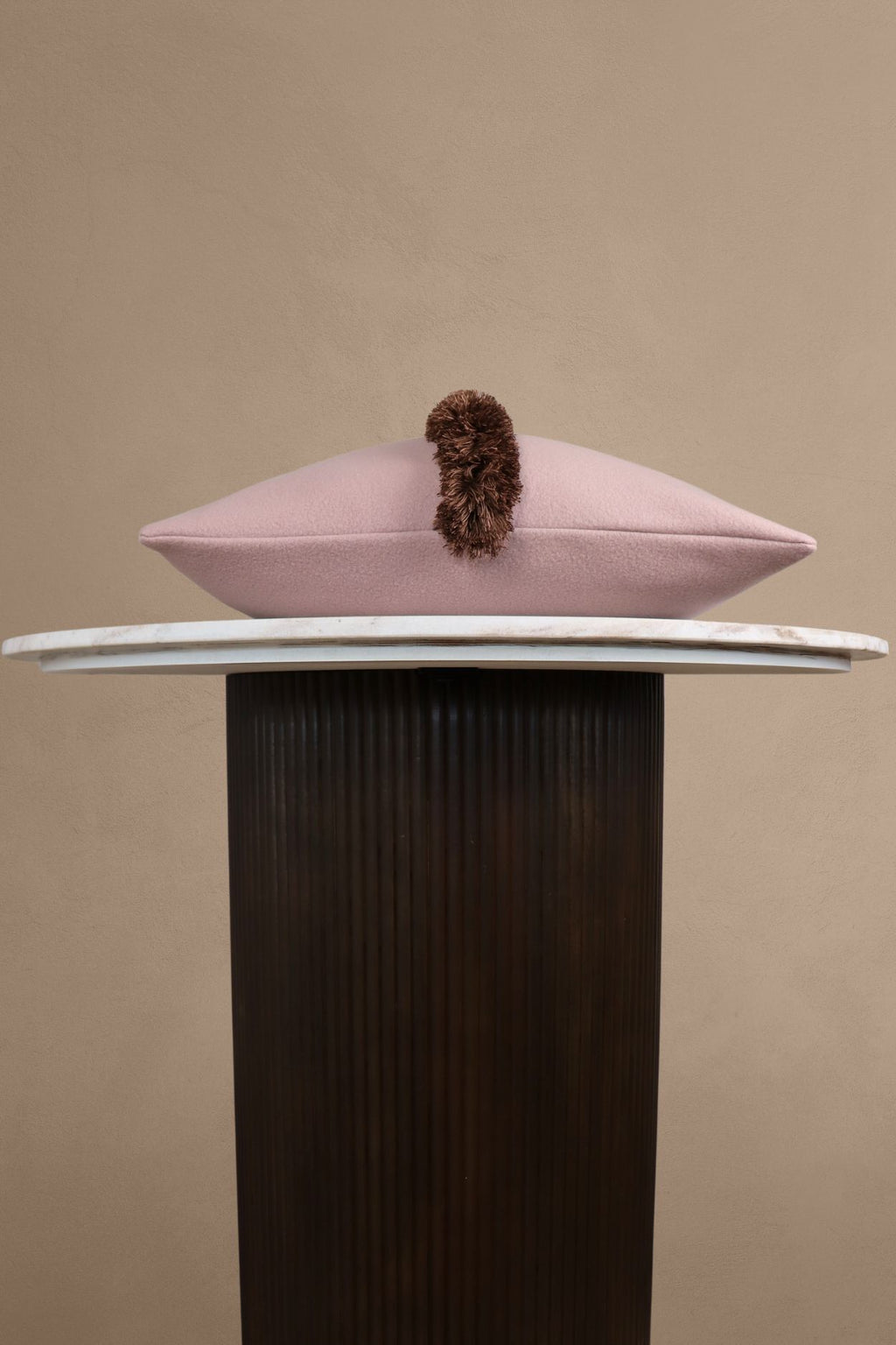 Een luxe roze sierkussen met bruine franjes ligt op een tafeltje.