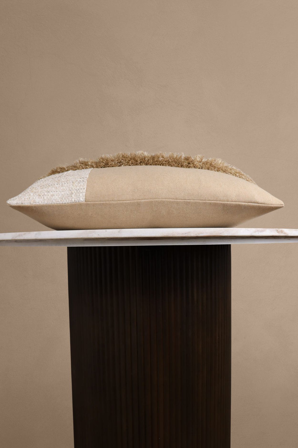 Een beige sierkussen met franjes ligt op een tafeltje.