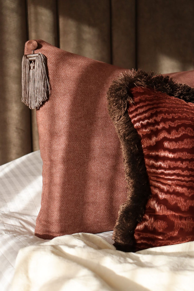 Twee roze sierkussens met franjes en kwastjes liggen op bed met een bruin hoofdbord.