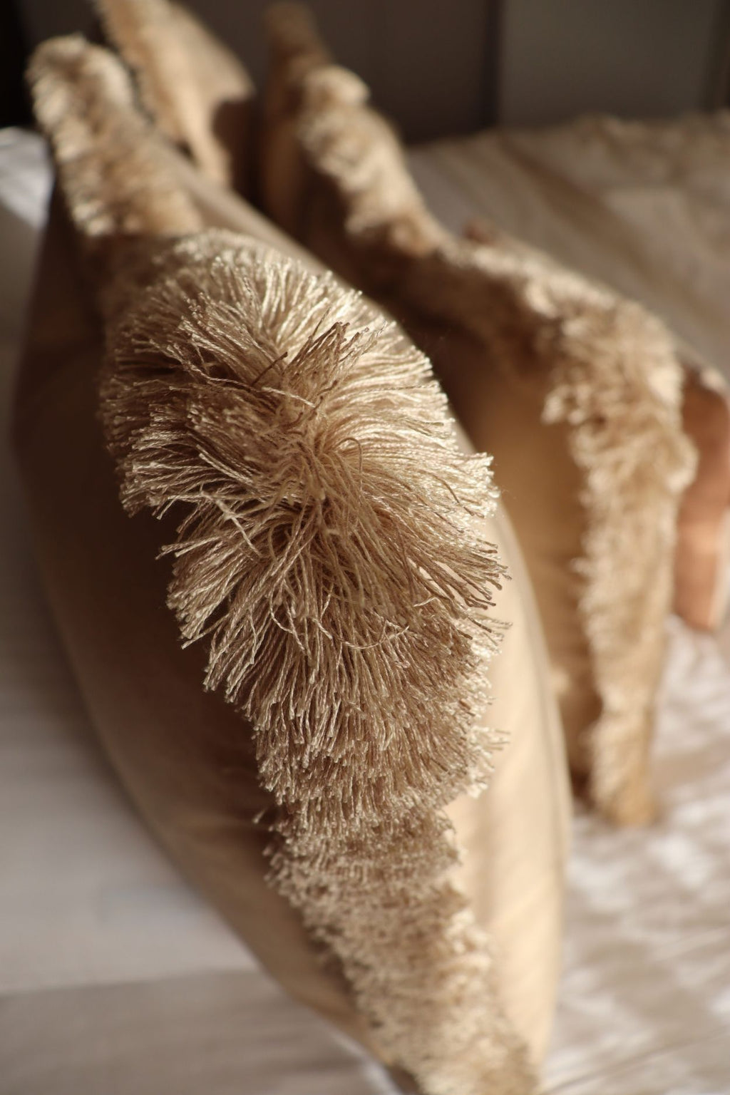 De beige franjes van een luxe groot sierkussen op bed.