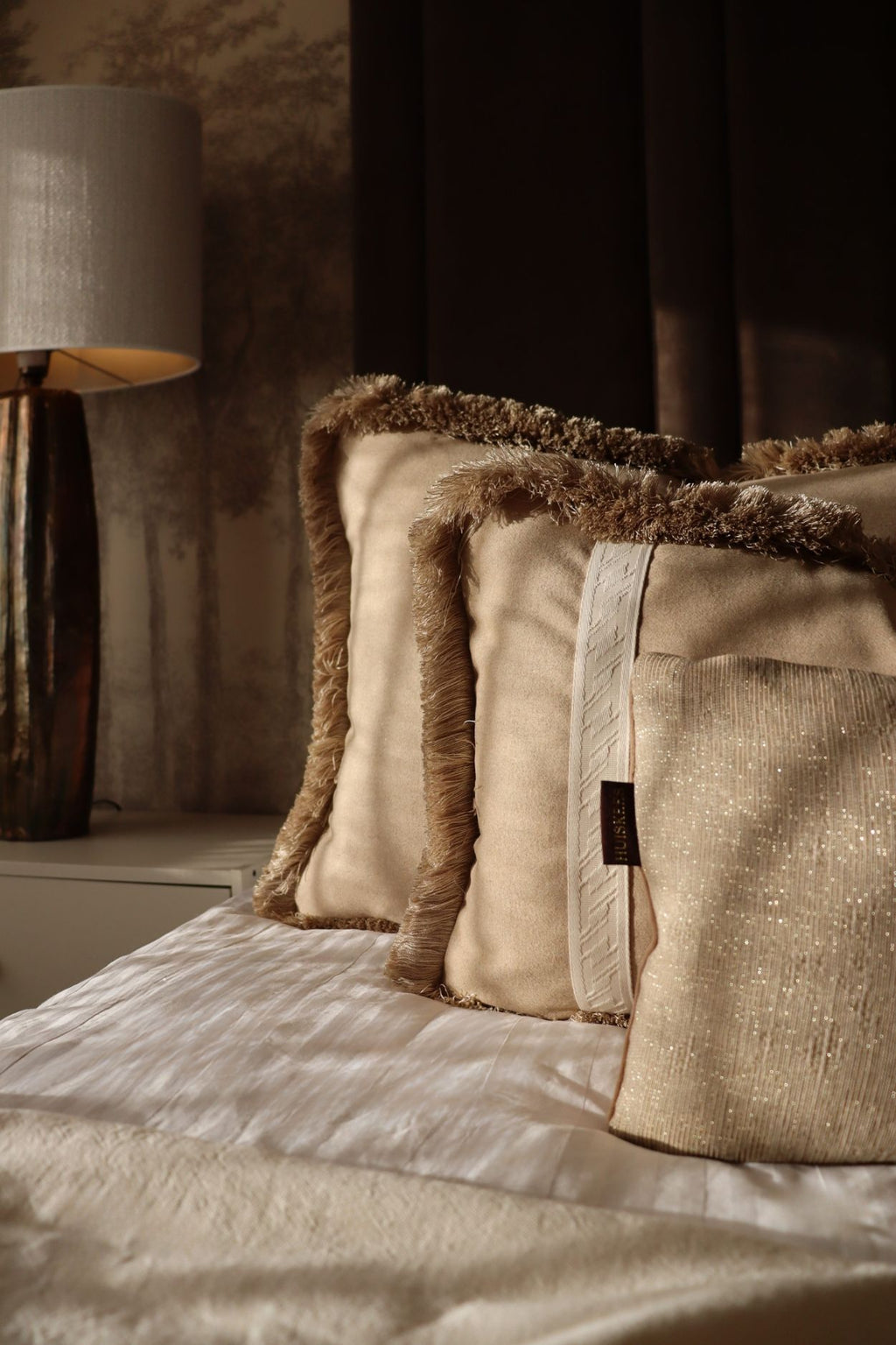 Een beige sierkussenset in grote formaten en franjes liggen op een luxe bed.