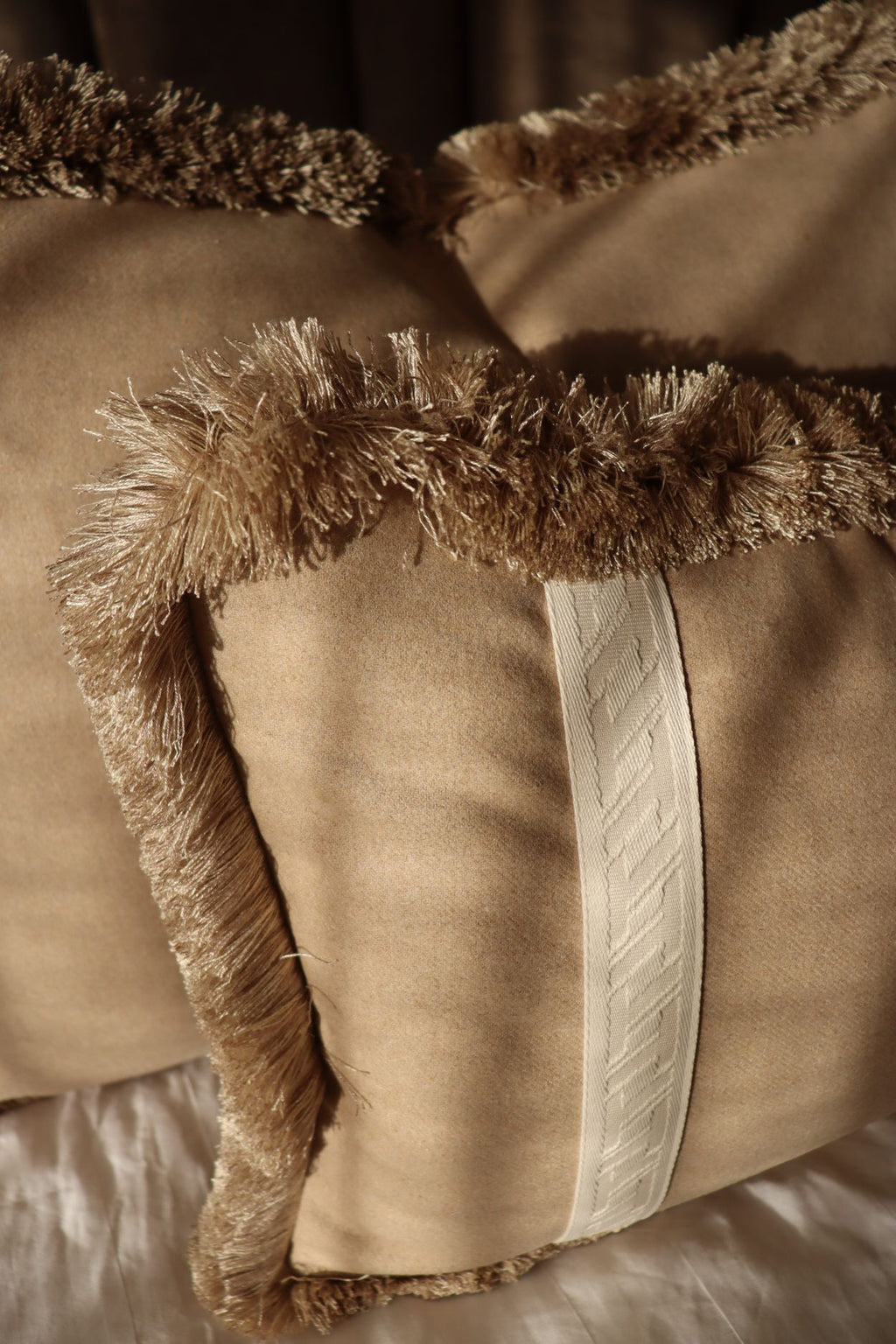 Een beige sierkussen met witte strook en beige franjes voor op bed.