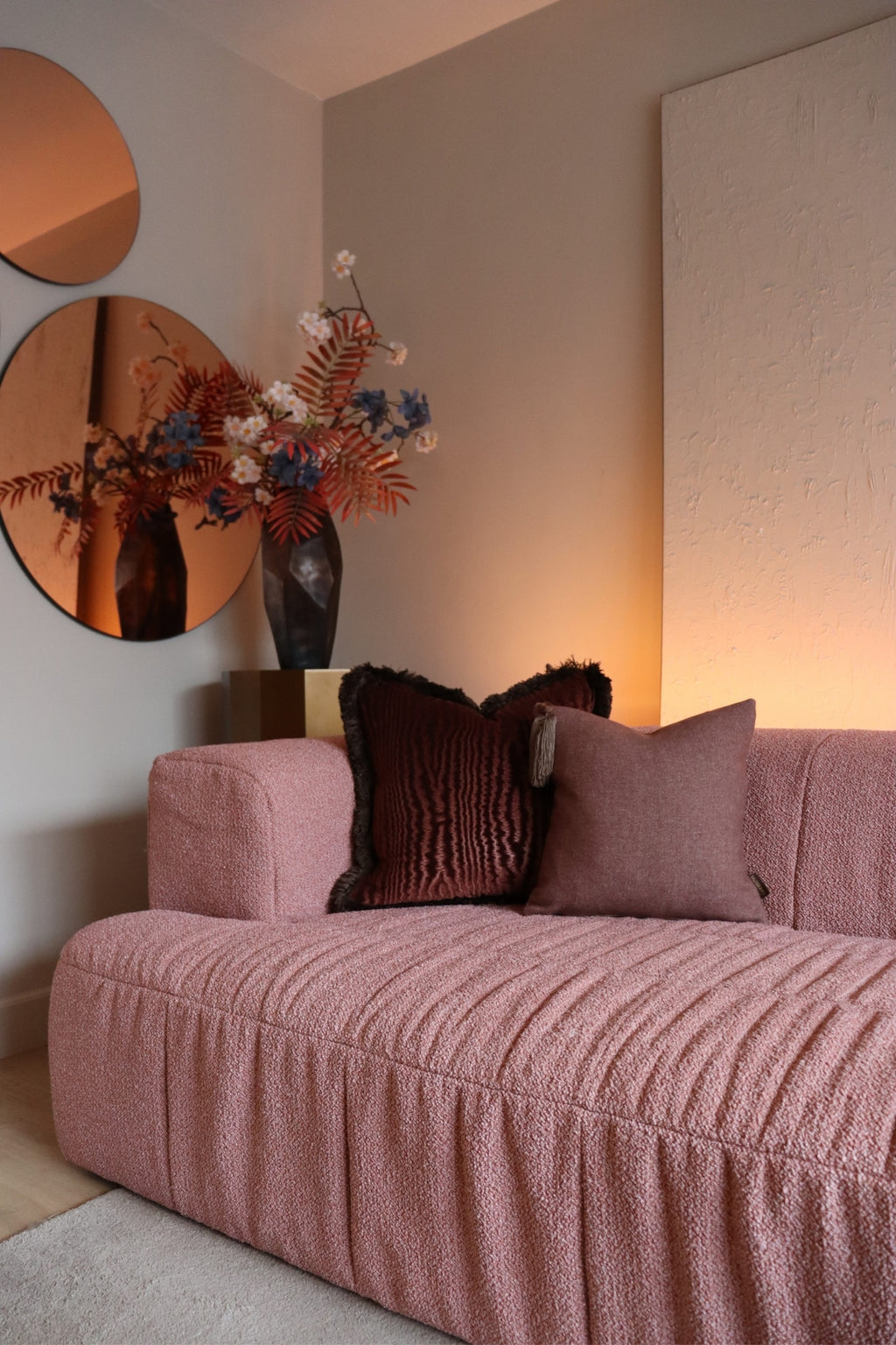 Twee donkerroze sierkussens met franjes en kwastjes op een roze bank.