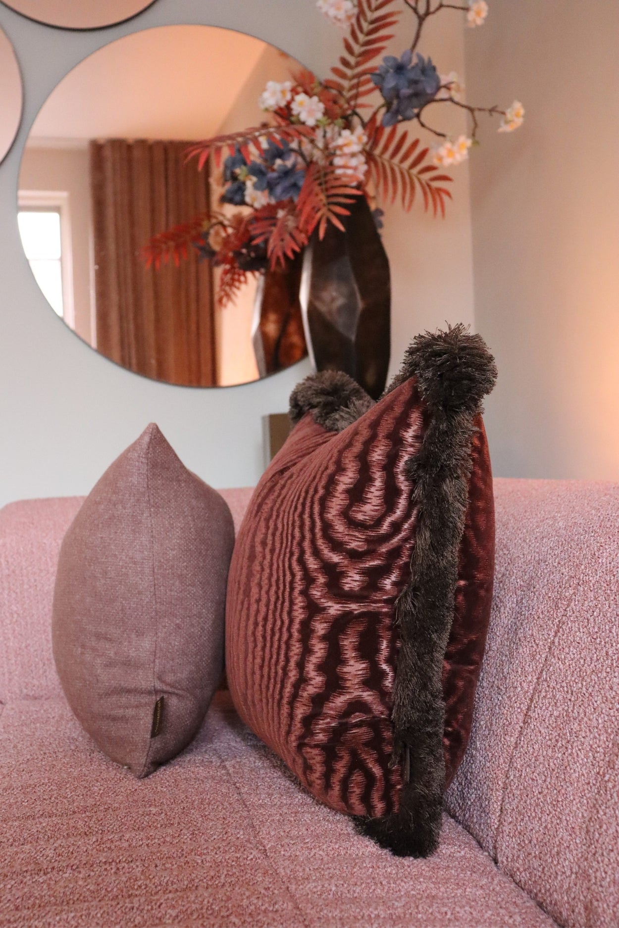 Twee donkerroze sierkussens met franjes en kwastjes op een roze bank.