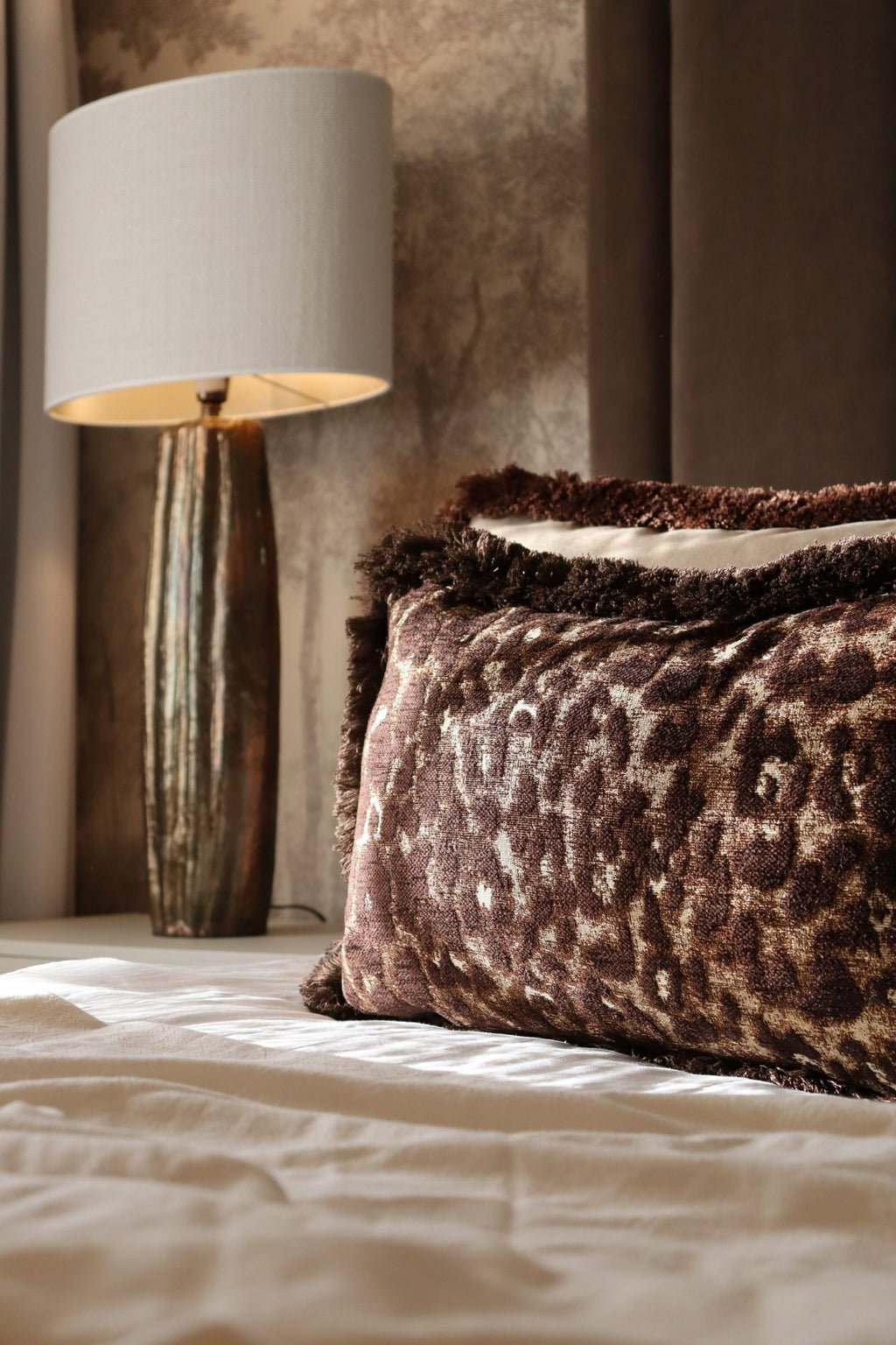 Een bruin sierkussen met luipaardmotief en bruine franjes ligt op bed.